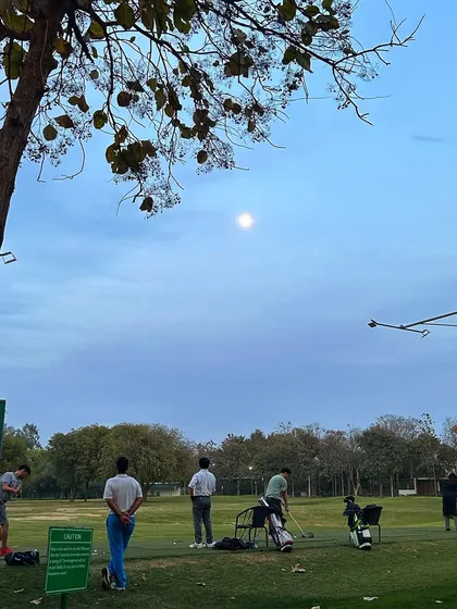 The moon watches over as a few dedicated golfers continue their practice into the evening.