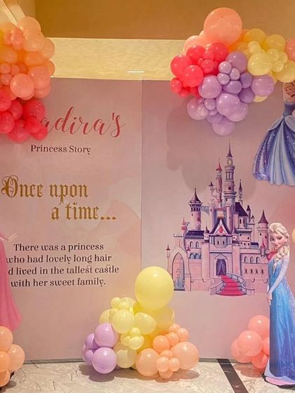 A Disney Princess "Once upon a time" storybook backdrop. The setup includes cutouts of various princesses like Cinderella, Elsa, and Aurora, surrounded by colorful balloon clouds.