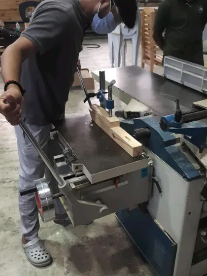A student operates the lever on a mortising machine to cut a clean mortise joint.