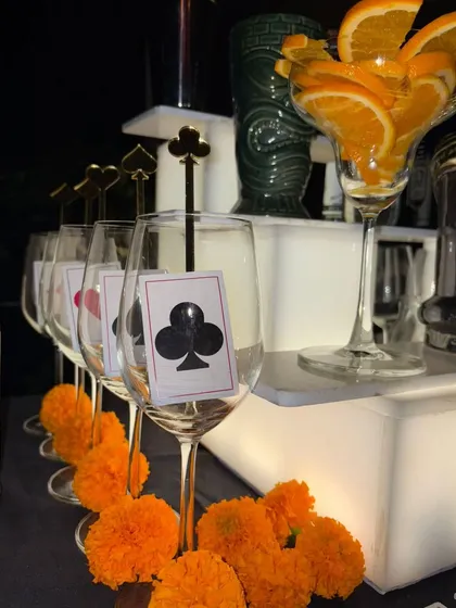 A casino-themed bar detail, with wine glasses marked with card suits and custom spade-shaped stirrers. The orange marigold garland adds a touch of traditional Indian decor.