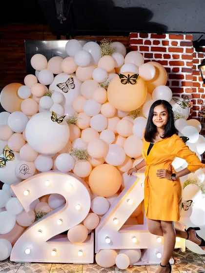 A chic 24th birthday setup with marquee numbers and a wall of white and peach balloons. The little butterfly details add a touch of whimsy to the elegant decor.