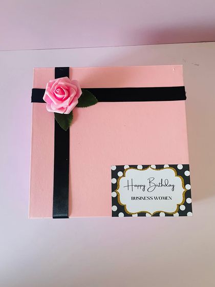 The exterior of the pink birthday box, showing the simple and elegant wrapping with a black ribbon and a custom name tag.