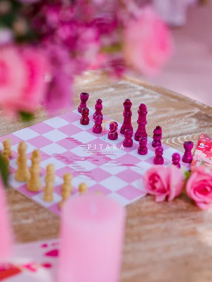 Checkmate. A close-up of the custom pink chessboard, surrounded by scattered rose petals and a soft pink candle. This detail was a huge hit with guests.