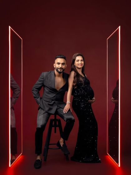 A bold and stylish couple's portrait against a red backdrop with glowing mirror frames, perfect for a high-fashion maternity look.