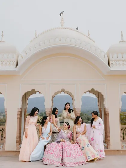 An elegant portrait of the bride seated with her bridesmaids against the backdrop of a beautiful palace dome and arches.