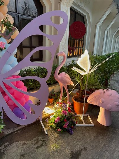 A close up of the outdoor decor elements, including a large pink butterfly wing prop, a flamingo, and a mushroom, creating an enchanted garden feel.