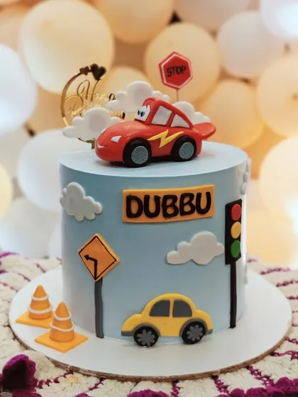 A cute car-themed cake with traffic signs and a fondant Lightning McQueen on top.