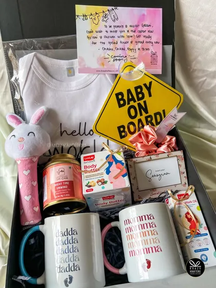 A complete 'Parents-to-Be' hamper, packed with essentials like 'Momma' and 'Dadda' mugs, a 'Hello World' onesie, body butter for mom, a baby rattle, and a 'Baby on Board' sign.