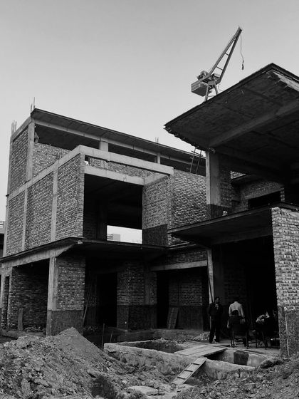 A construction site view showing the exposed brick and concrete frame of a large residence. The crane in the background is a testament to the scale of the project, which we manage from the first dig to the final detail.