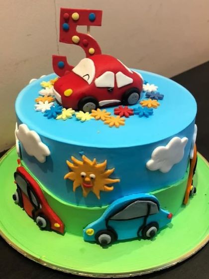 A vibrant car-themed cake for a 5th birthday. The bright blue and green layers are decorated with fun, colorful fondant cars, making it a dream for any little racer.