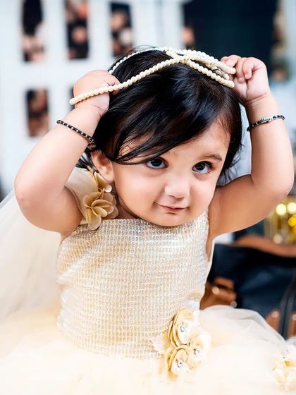 A little girl plays with a string of pearls, lifting them like a crown in this adorable and chic portrait.