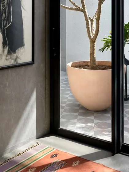 Sunlight casts dramatic shadows across the floor, highlighting the texture of the wall and the simple elegance of the decor. This view into a courtyard shows how we use natural light as a key design element.