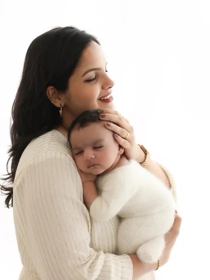 The soft glow of new motherhood. This portrait focuses on the quiet bond and overwhelming love a mother feels. The simple, light-filled setting emphasizes the pure emotion of the moment.