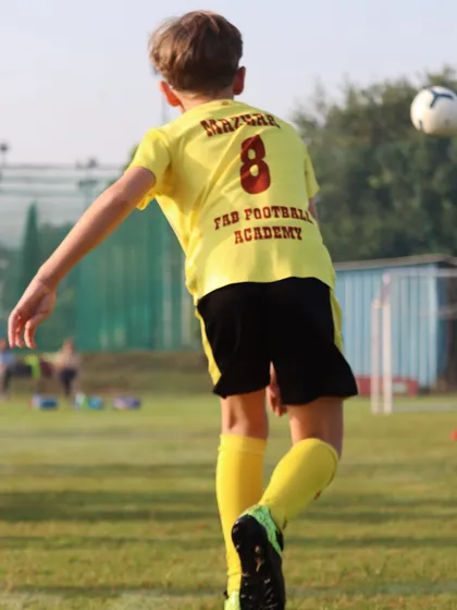 A player in our yellow kit strikes the ball. Our holistic development includes regular matches, 1-on-1 training, and camps to enhance skills.