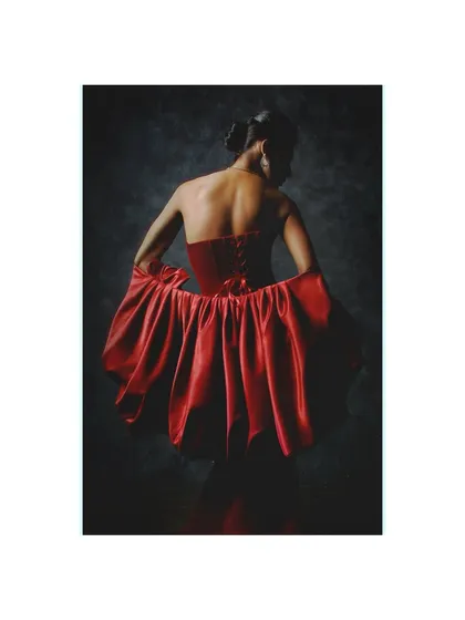 A view of the back of the red Ambika Lal gown. The styling focuses on the corset lacing and the beautiful drape of the satin, creating an image of quiet, romantic elegance.