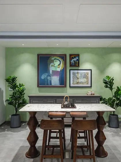 The 'Sepalika' office features a calm green accent wall adorned with a gallery of Indian art. The space is designed to feel like home, with comfortable furniture and personal touches.