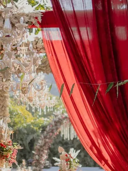 A detail shot of the rich red drapery and crystal chandeliers from our 'Regal Rustic Reverie' wedding. The combination of textures and light created a truly luxurious and romantic atmosphere.