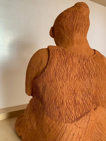 The back view of the terracotta sculpture, showing the intricate texture of the clothing and hair.