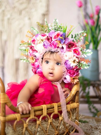 A sweet pose from a floral-themed sitter session. The baby looks adorable in her pink dress and flower crown, sitting in a rustic basket.
