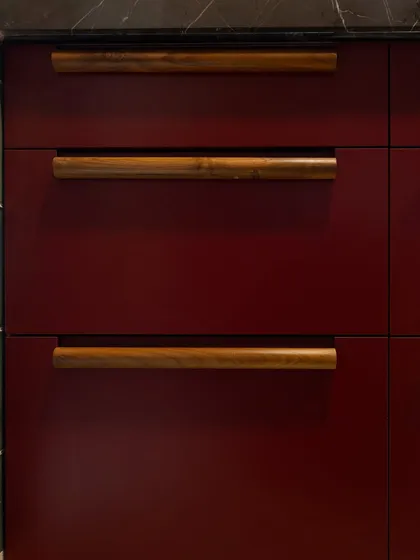 The texture and warmth of the wooden handles are a key feature in this kitchen. They are not just functional but are a design element in themselves, adding a layer of craftsmanship and softening the bold red of the cabinetry.