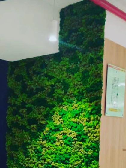 An L-shaped green wall installation in a commercial space. The bright green moss-like texture adds a vibrant splash of color to the corner.