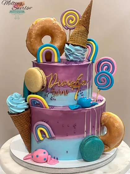 A two-tier candy-themed cake in purple and blue, made for our daughter's birthday. It's loaded with donuts, macarons, and handmade fondant candies.