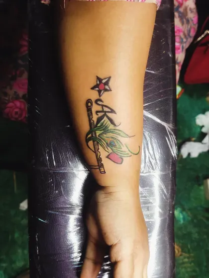 A clear look at the finished 'A' initial tattoo, which incorporates a star, Krishna's flute, and a peacock feather with hints of color for a unique spiritual design.
