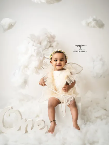 A little angel with the sweetest smile, sitting on a fluffy cloud. This heavenly setup with wings and a halo is perfect for a dreamy and ethereal portrait.