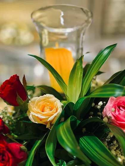 A close-up of a classic centerpiece with yellow and red roses and a candle, perfect for adding a touch of warmth and color to any table.
