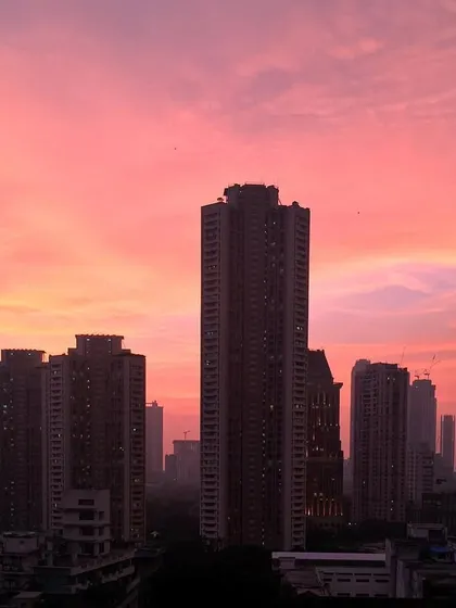 A soft pink and orange sunset glows behind the silhouette of Mumbai's skyscrapers, captured with an iPhone.
