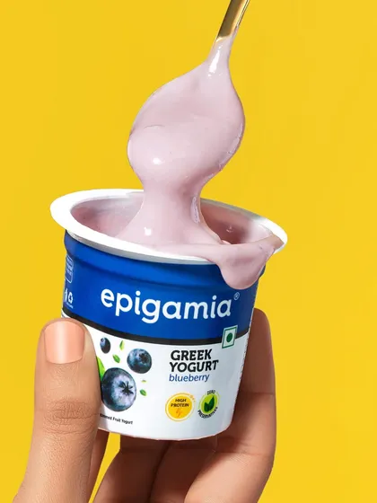 A slightly different angle of the Epigamia blueberry yogurt scoop. This shot emphasizes the glossy, smooth drip of the yogurt, making it look incredibly delicious and appealing.