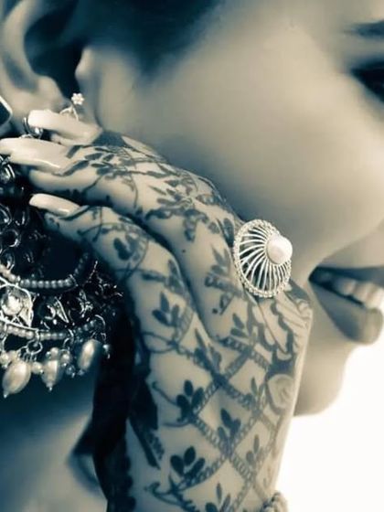 A close-up, artistic shot focusing on the bride's hands, adorned with intricate mehndi, as she puts on her heavy traditional earring. It’s a beautiful detail shot that tells a story of preparation.