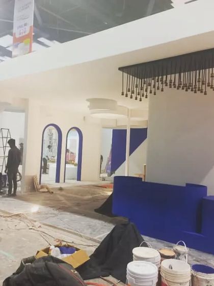 A behind-the-scenes look at a modern booth being set up, featuring elegant archways and a deep blue reception desk.