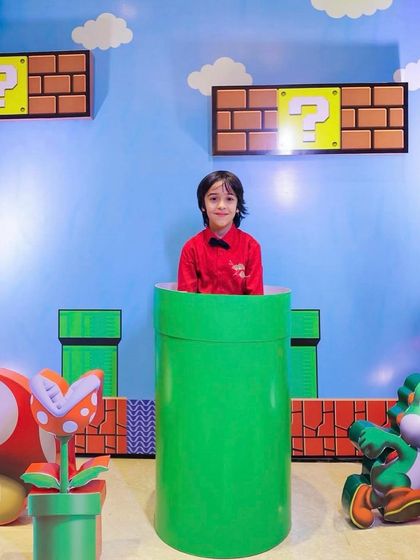 It's-a me, Mario! A young guest enjoys the interactive warp pipe photo op at our Super Mario themed party. The backdrop features the classic sky and question blocks from the game.
