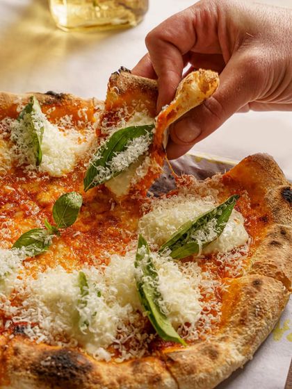 A classic Margherita pizza, with a slice being lifted. The focus is on the thin crust and the fresh basil and cheese toppings. The lighting gives it a warm, inviting glow.