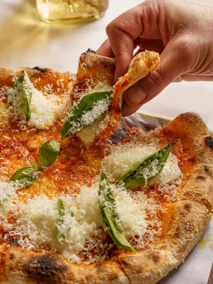 A classic Margherita pizza, with a slice being lifted. The focus is on the thin crust and the fresh basil and cheese toppings. The lighting gives it a warm, inviting glow.