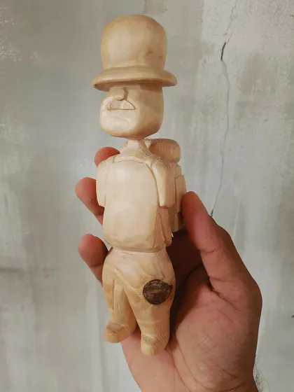 A front view of our little wooden traveler. You can see the details of his mustache and backpack, all hand-carved with care and a touch of whimsy.