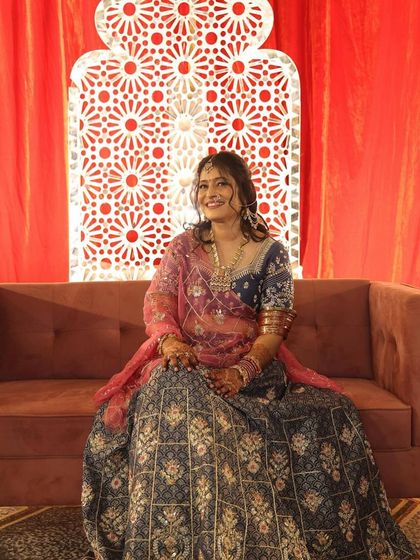 Our client looking regal and happy during her Mayra ceremony, seated in a deep blue and gold patterned lehenga with a contrasting pink dupatta.