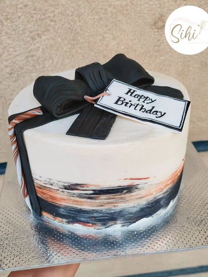 A modern and artistic birthday cake. This design features abstract brushstrokes of color and is topped with a stylish black fondant bow and gift tag.
