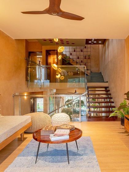 The informal living area on the upper floor is a cozy retreat. A comfortable daybed, woven poufs, and a simple wooden media console create a relaxed atmosphere. The space overlooks the central atrium, maintaining a sense of connection to the rest of the home.