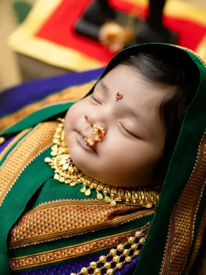 A sweet close-up of a newborn in a traditional Marathi saree wrap, highlighting the tiny nose ring and peaceful expression.