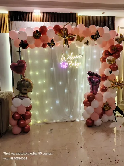 An elegant "Welcome Baby" setup with a balloon arch over a fairy light curtain, perfect for a stylish homecoming.