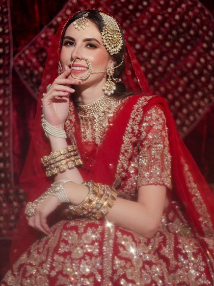 A beautiful bride in a sparkling red lehenga, her hair neatly styled to showcase her radiant smile and stunning jewelry.