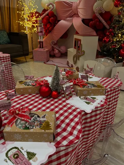 The kids' table at the Christmas party was filled with festive return gifts and decor, set against the warm glow of the main party setup.