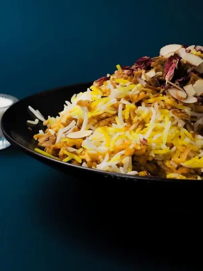 A beautifully presented bowl of biryani, garnished with fried onions, nuts, and rose petals, with raita on the side. This image captures the artistry and flavor I put into every dish.