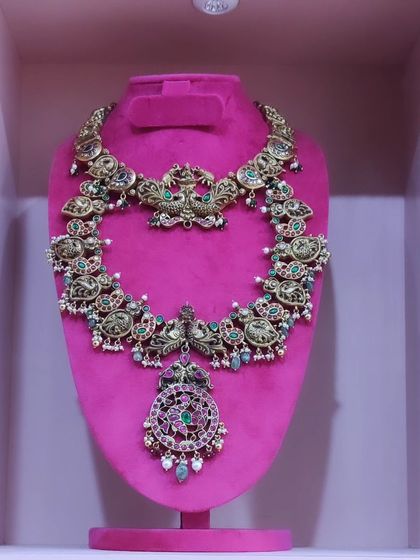 A close-up of a beautiful antique finish haram with intricate carvings and a ruby and emerald pendant.