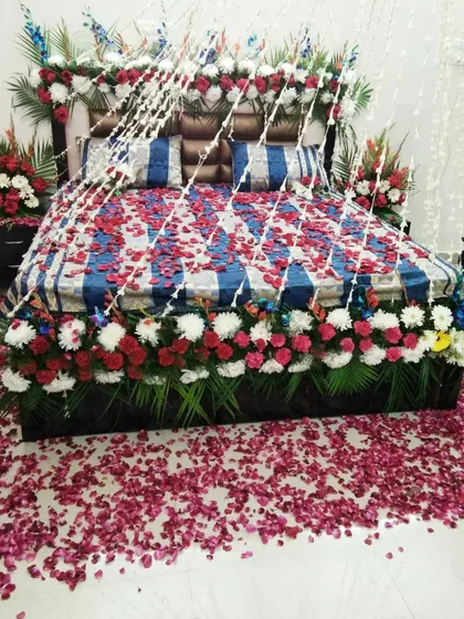 I provide special decoration for the bridal room for the first night. This lavish setup includes fresh flowers covering the bed and headboard, with rose petals scattered on the floor for a truly romantic feel.