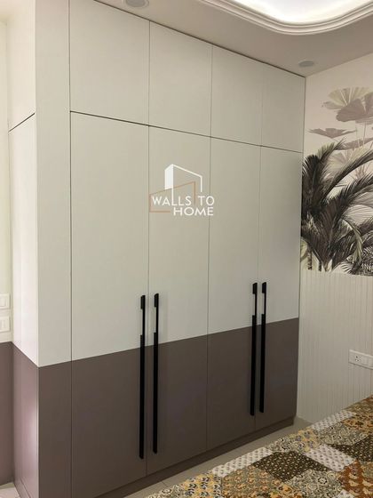 A two-tone, floor-to-ceiling wardrobe with sleek black handles. This design provides ample storage while maintaining a modern aesthetic that complements the room's decor.