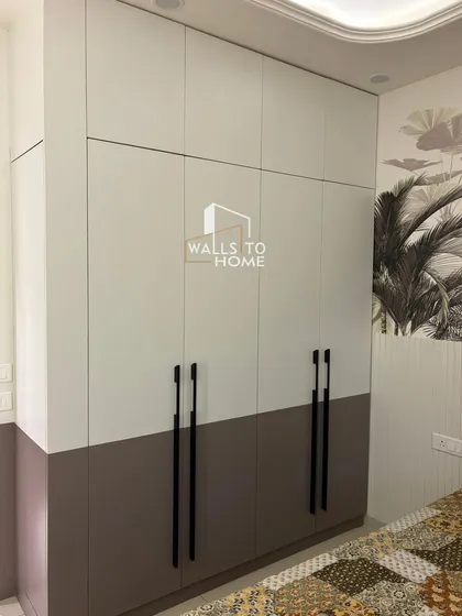 A two-tone, floor-to-ceiling wardrobe with sleek black handles. This design provides ample storage while maintaining a modern aesthetic that complements the room's decor.