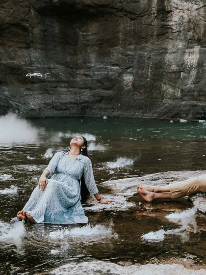 A couple relaxing by a serene waterfall, with a drone visible in the frame, showcasing the use of modern technology to capture unique angles.